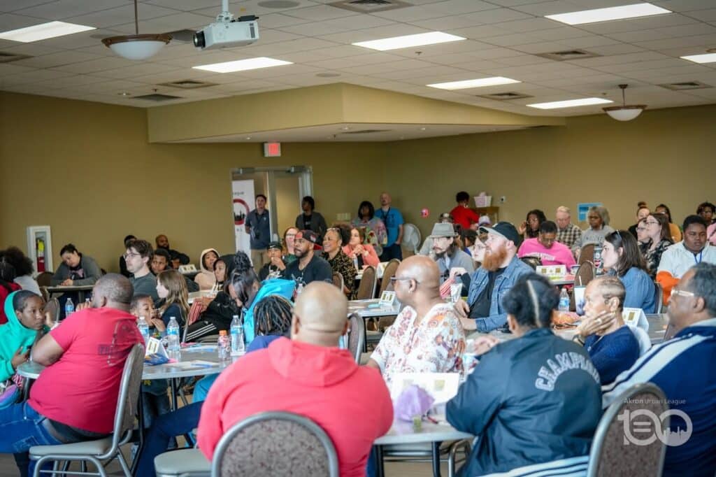684572757_18226207420314357_8075846361784429357_n-1024x682 | Akron Urban League Large Group of Diverse People Seated at Round Tables in a Conference Room, Attending a Community Event with a Projector Overhead Above Them (informational).