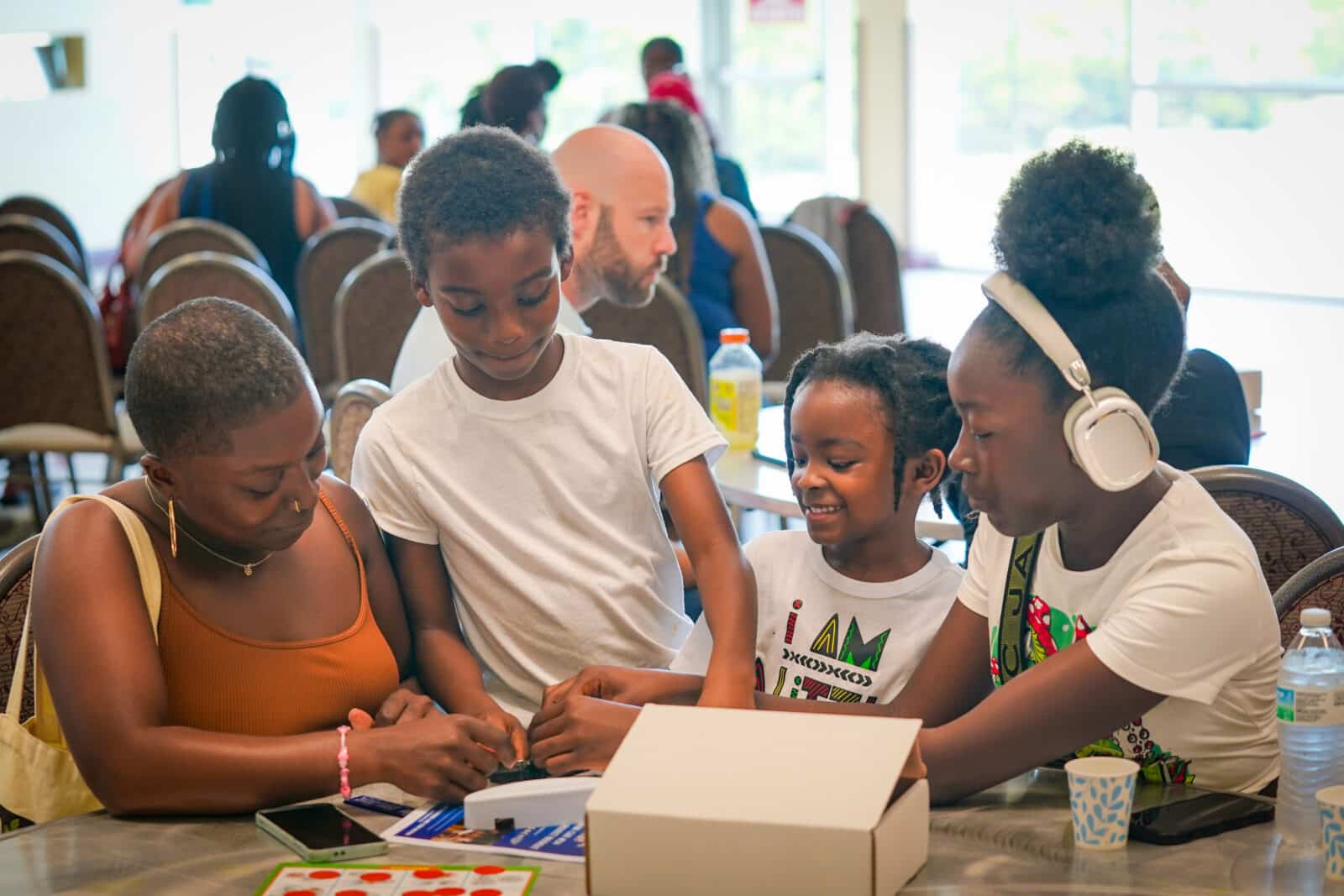 Woman and three children gathered around a table, focused on an activity with a white box.