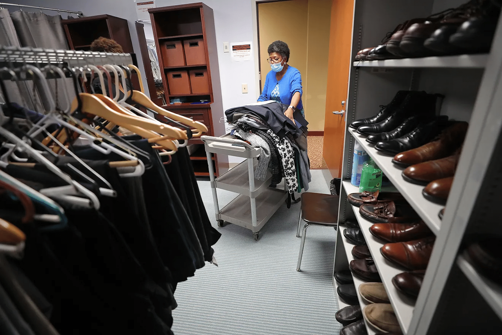 Career Clothing Closet-JeffLangeAkronBJ-Credit | Akron Urban League Bald Man with Beard in a Black Shirt Speaks to a Woman with Arm Tattoos Holding a Pen, Near a Projected Slide.