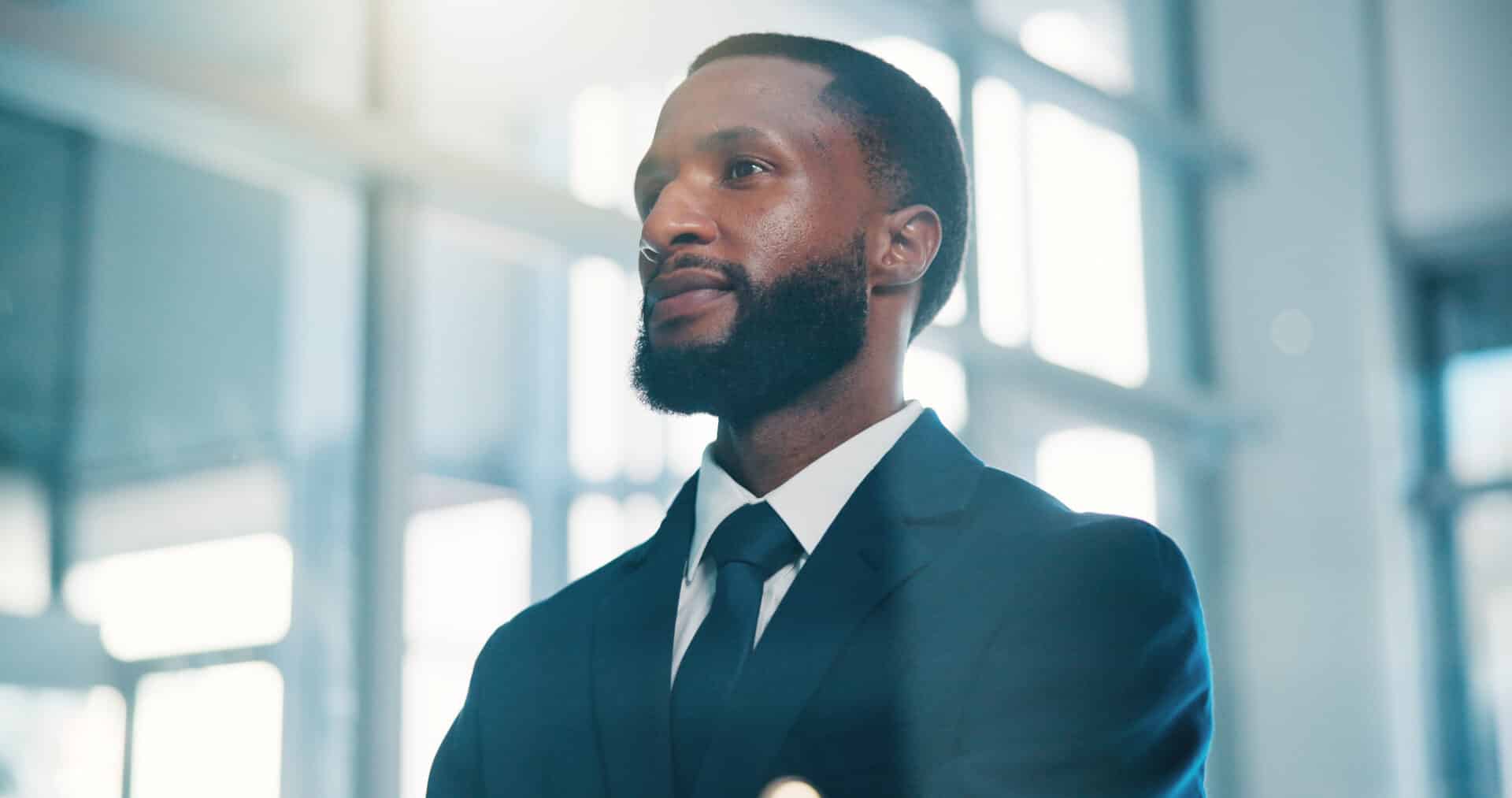 Portrait of a Bearded Man in a Dark Suit and Tie, Looking Upward in a Bright, Modern Office Hallway