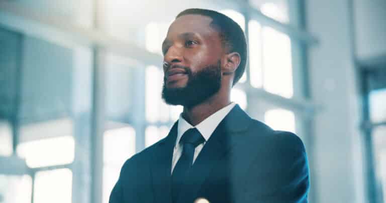 Portrait of a Bearded Man in a Dark Suit and Tie, Looking Upward in a Bright, Modern Office Hallway