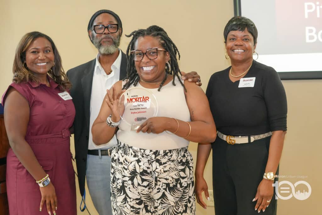 Dsc00545-1024x683 | Akron Urban League Four People Stand Together at an Award Ceremony; the Center Woman Holds a Translucent Mortar Award and Smiles at the Camera.