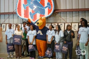 Group of Teens with a Dog Mascot Posing for a Photo at a Soapbox Derby Summer Camp Event, Each Holding Goodie Bags.