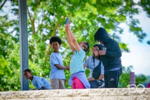 Children on an Outdoor Stage Celebrate As One Girl Raises a Trophy High with Friends Applauding Nearby, Sunny Green Park in Background.