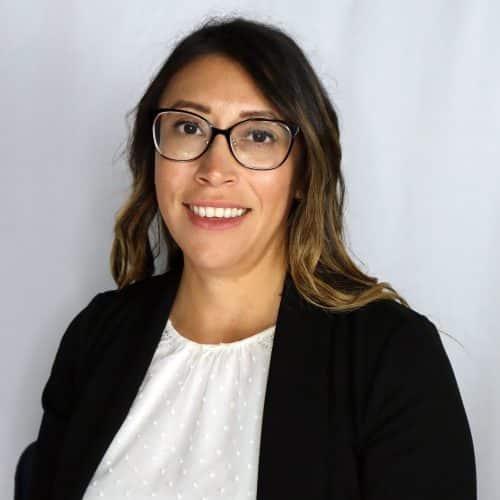 Professional headshot of a woman with glasses, shoulder-length hair, wearing a black blazer and white blouse, smiling at the camera.