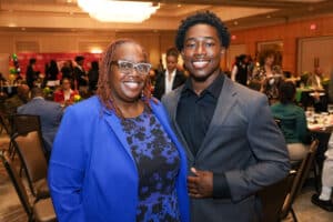Img_0724-300x200 | Akron Urban League Two Smiling Attendees Posing for a Photo at a Formal Dinner Event; Woman in a Blue Blazer and Patterned Dress, Man in a Dark Suit, Banquet Hall in the Background.