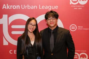Img_0750-300x200 | Akron Urban League Two Young Adults in Formal Attire Pose for a Photo at an Akron Urban League Event, Standing in Front of a Red Backdrop with Logos.