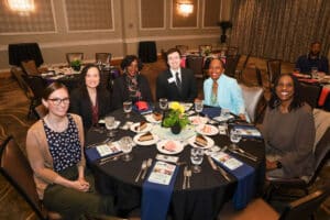 Img_0759-300x200 | Akron Urban League Seven Professionals Sit Around a Round Banquet Table at a Formal Event, Smiling for the Photo with Place Cards and a Centerpiece Centerpiece on the Table.