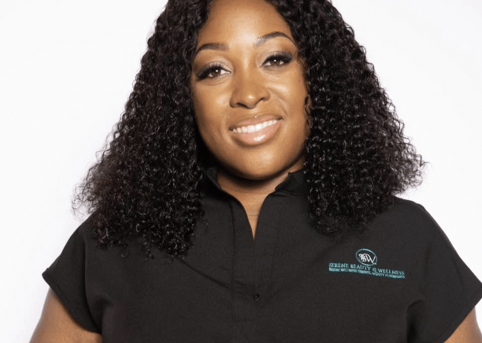Smiling Black woman with shoulder-length curly hair, wearing a black polo shirt with a turquoise Serene Beauty & Wellness logo on the chest.