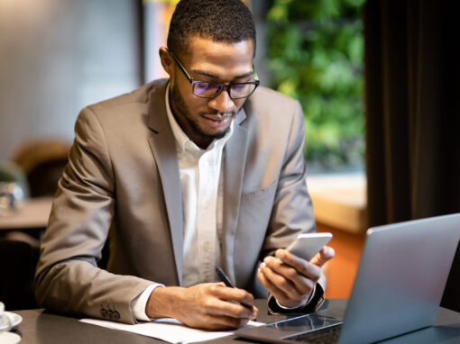 Black business guy taking notes in notebook holding phone