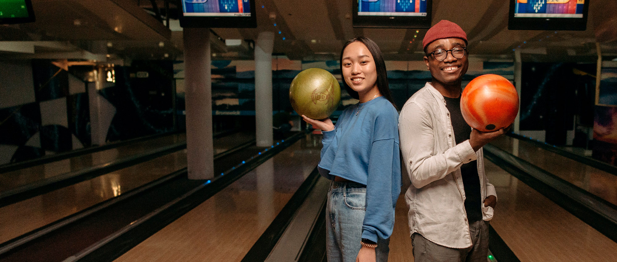 Young Asian woman and Black man posing with bowling balls