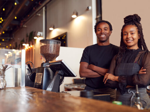 Portrait Of Male And Female Coffee Shop Owners Standing At Sales Desk