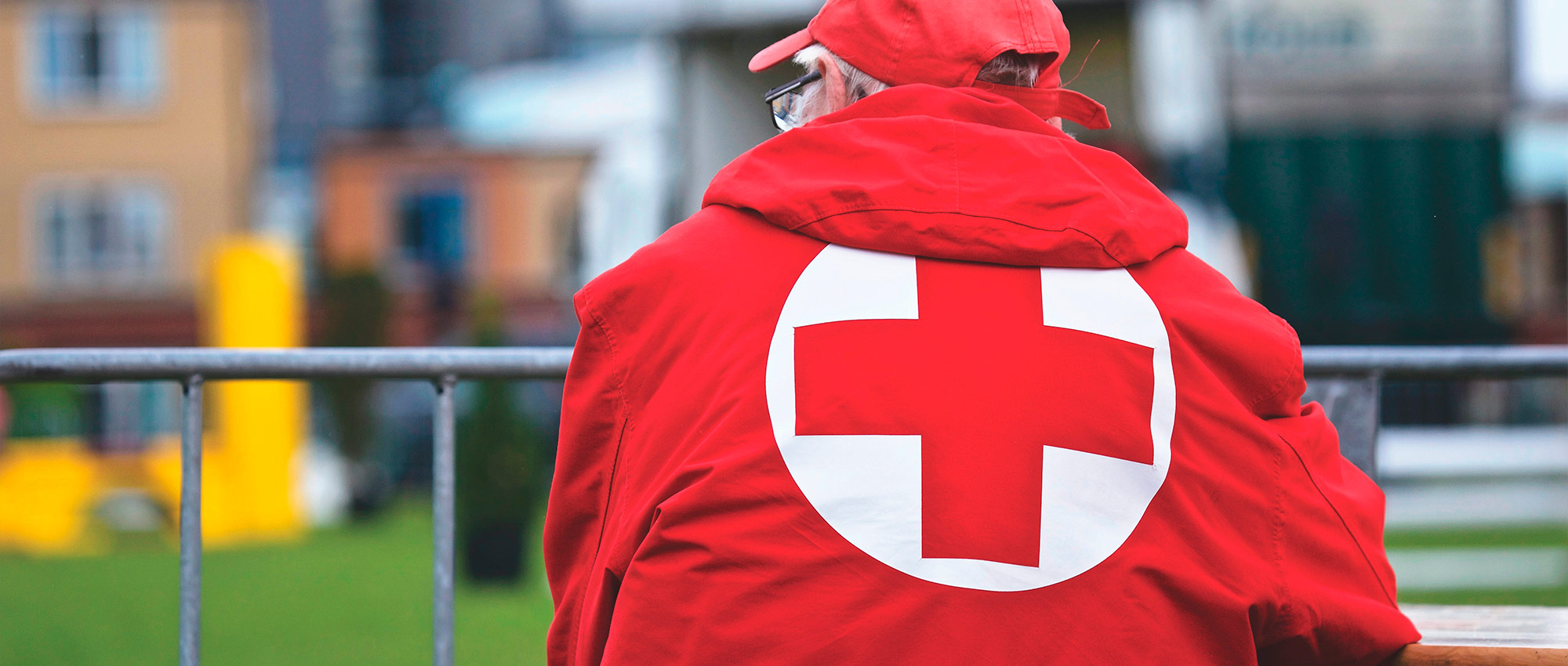 Man in a Red Cross jacket leaning over a fence
