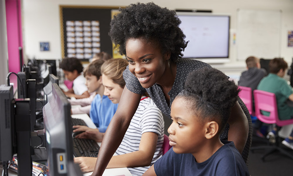 Teacher Helping Female Pupil Line Of High School Students Working at Screens In Computer Class
