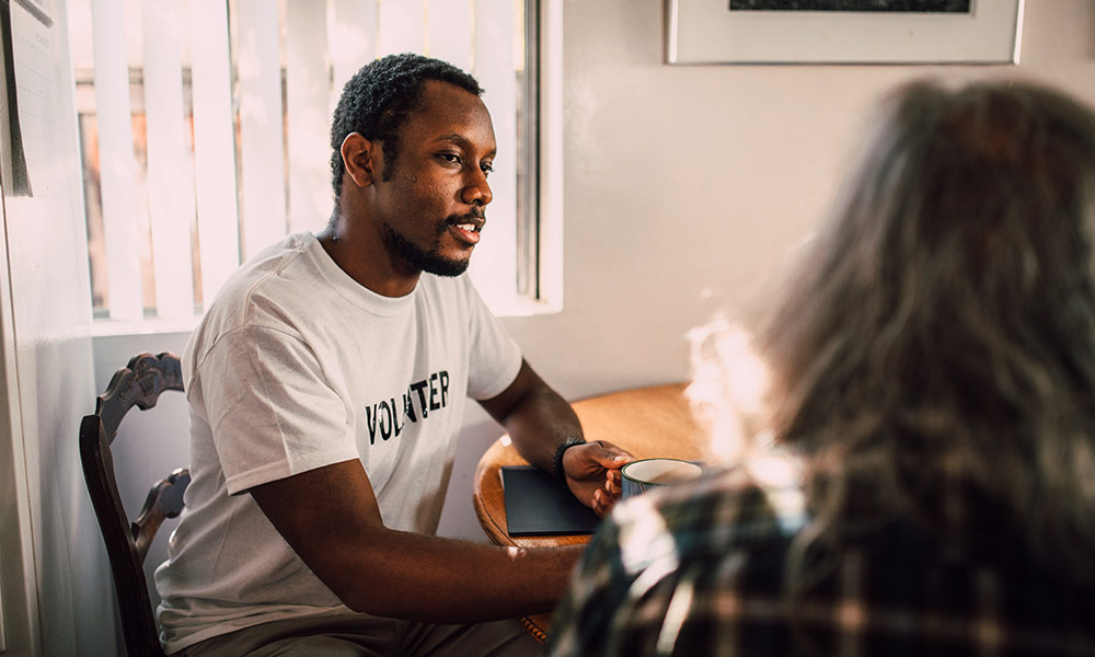 Young Black volunteer sitting with an elderly person