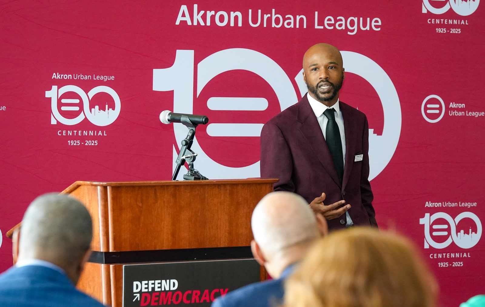 voter-rights-compressed | Akron Urban League Bald Man with Beard in a Black Shirt Speaks to a Woman with Arm Tattoos Holding a Pen, Near a Projected Slide.